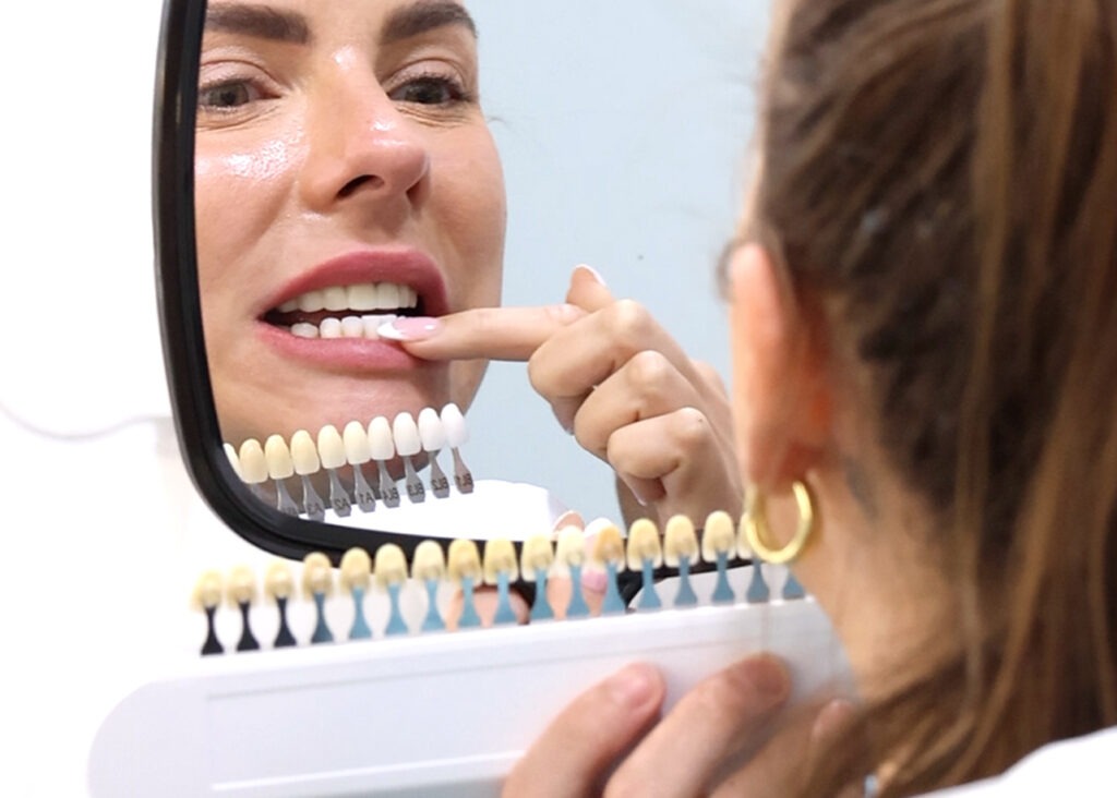 A woman comparing tooth shades while looking in a mirror